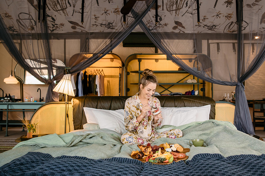 Woman has breakfast in bed at Saseka Tented Camp‍ in Kruger National ⁣Park,​ South ​Africa.